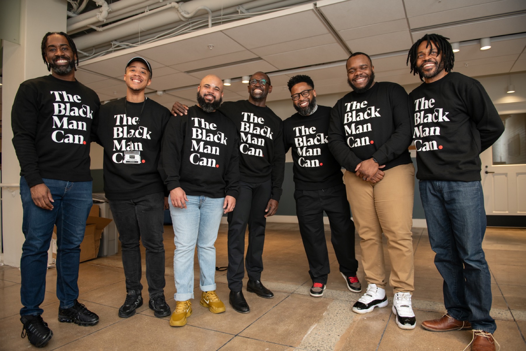 Seven Black male educators in The Black Man Can shirts standing together